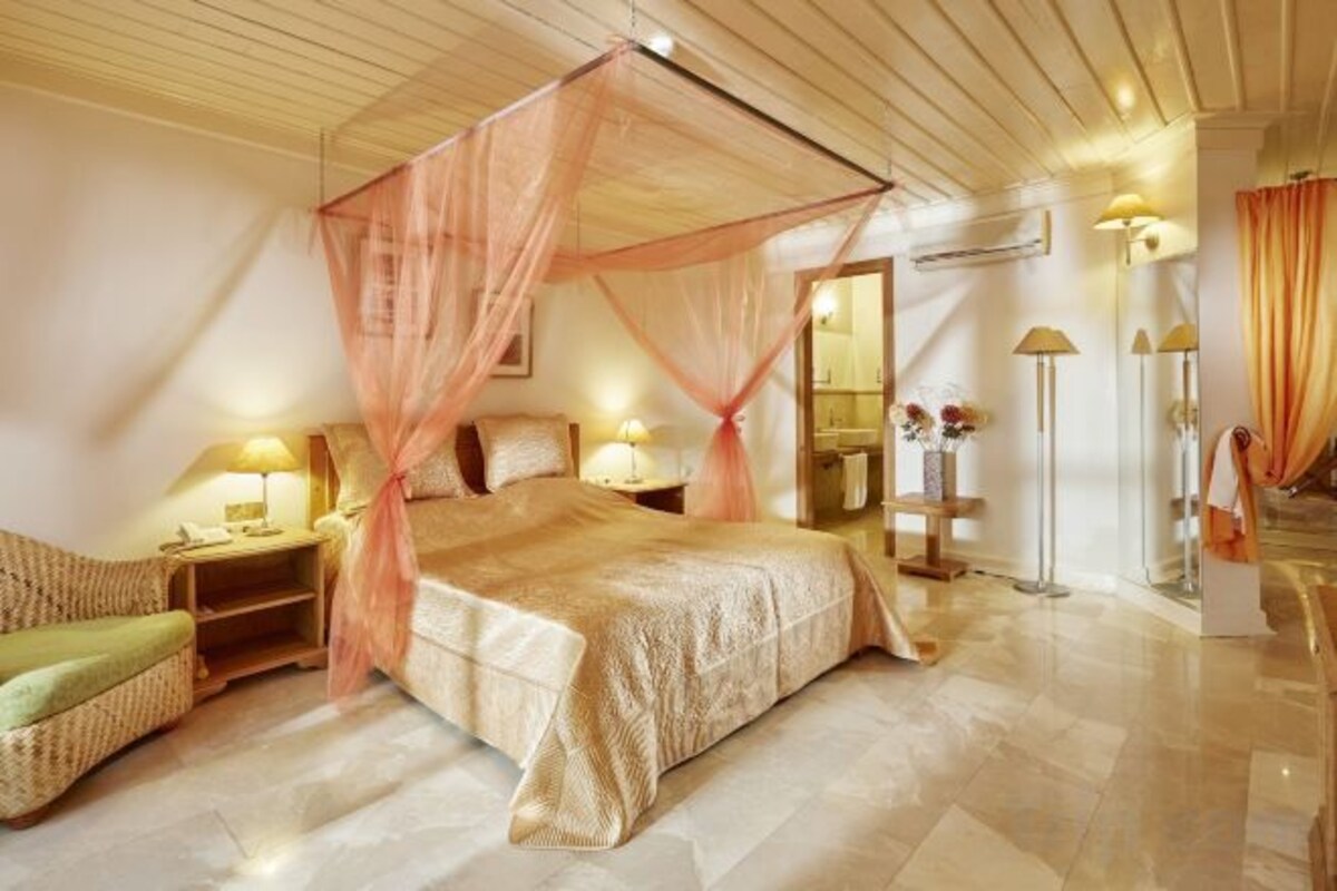A bedroom with a canopy bed, bedside lamps, a green chair, and a mirror.