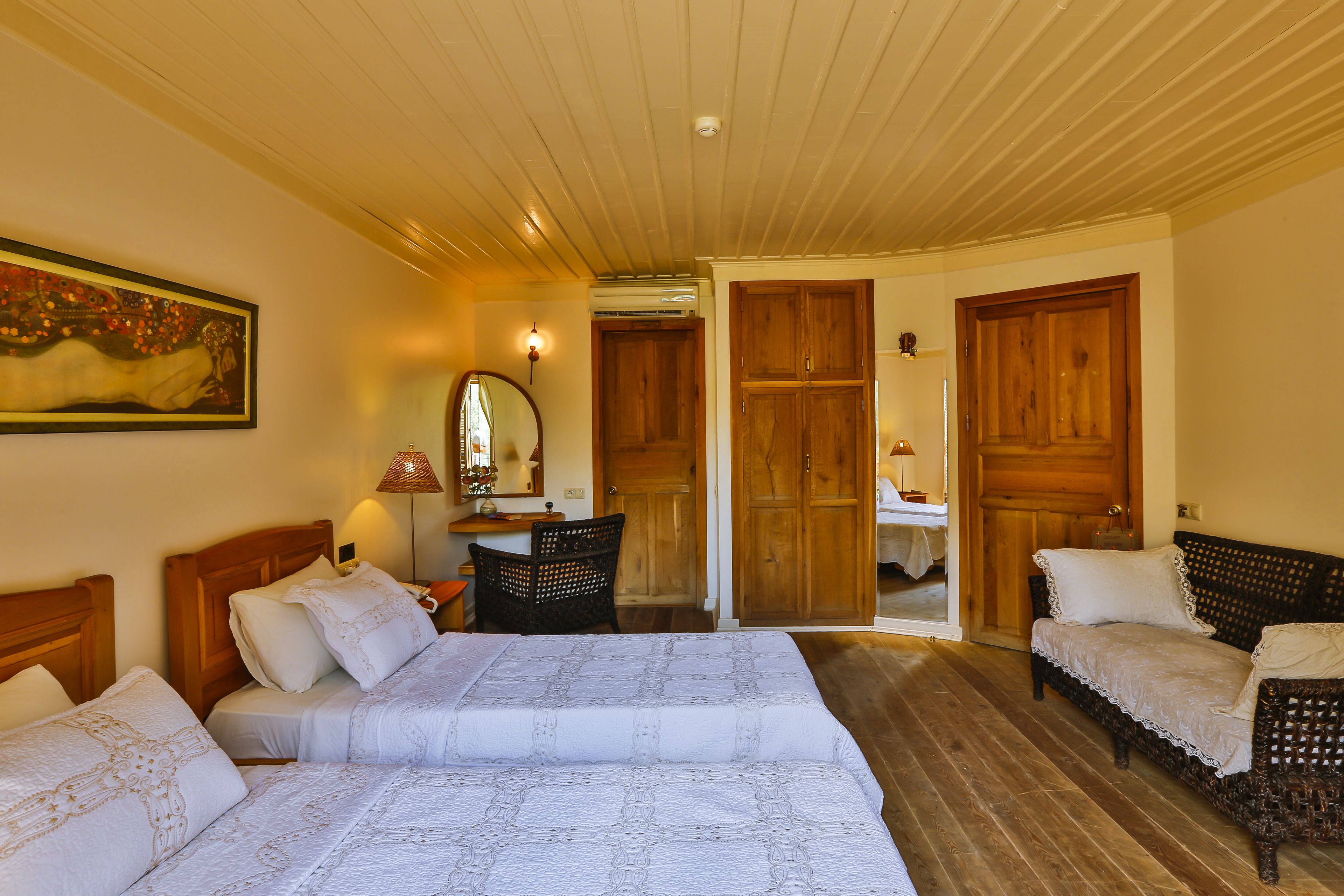 A bedroom with two beds, a wooden wardrobe, a mirror, and a wicker chair.