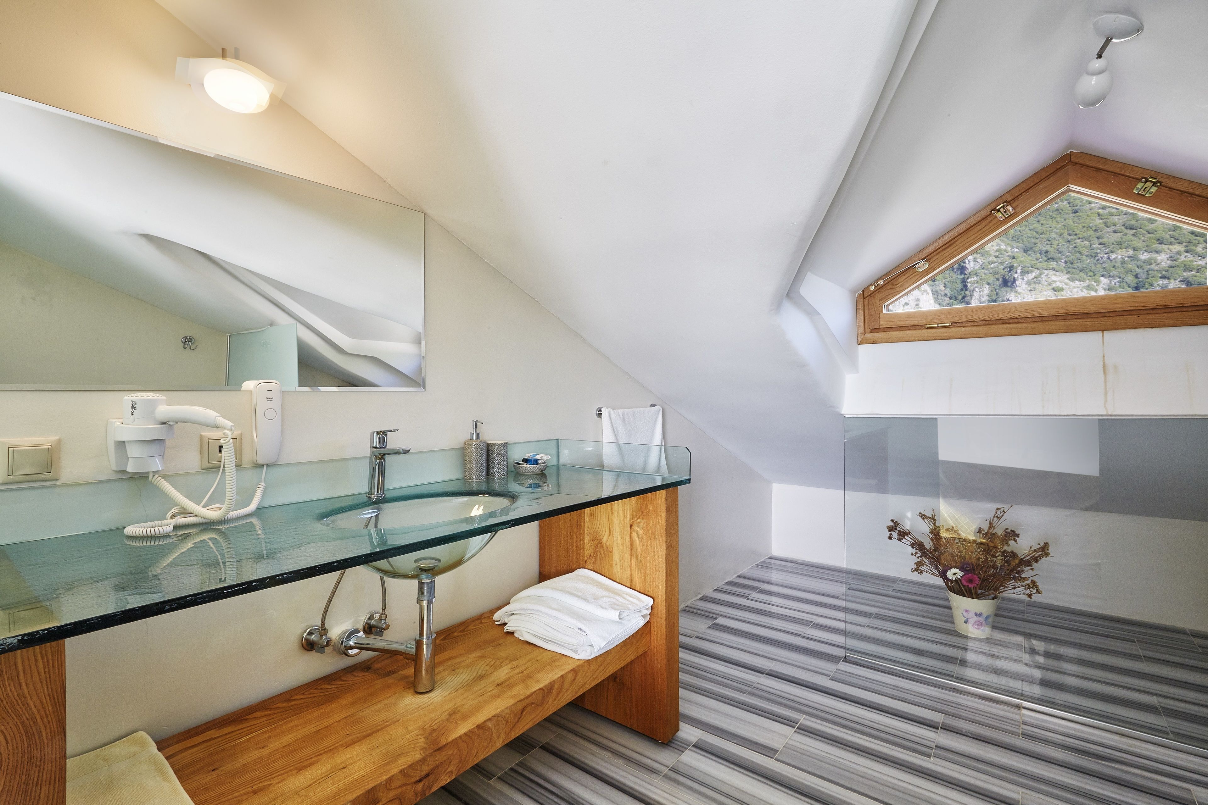A modern bathroom with a glass sink, wooden vanity, and a skylight.