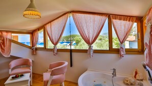 Una habitación con un ventanal grande, una bañera con flores y dos sillas rosas.