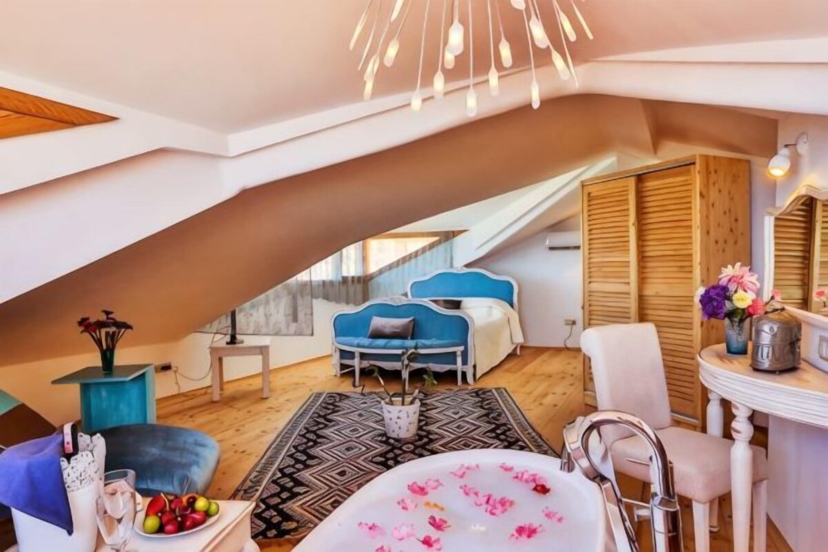A modern bedroom with a sloped ceiling, a blue bed, a wooden wardrobe, and a bathroom with a bathtub and a sink.