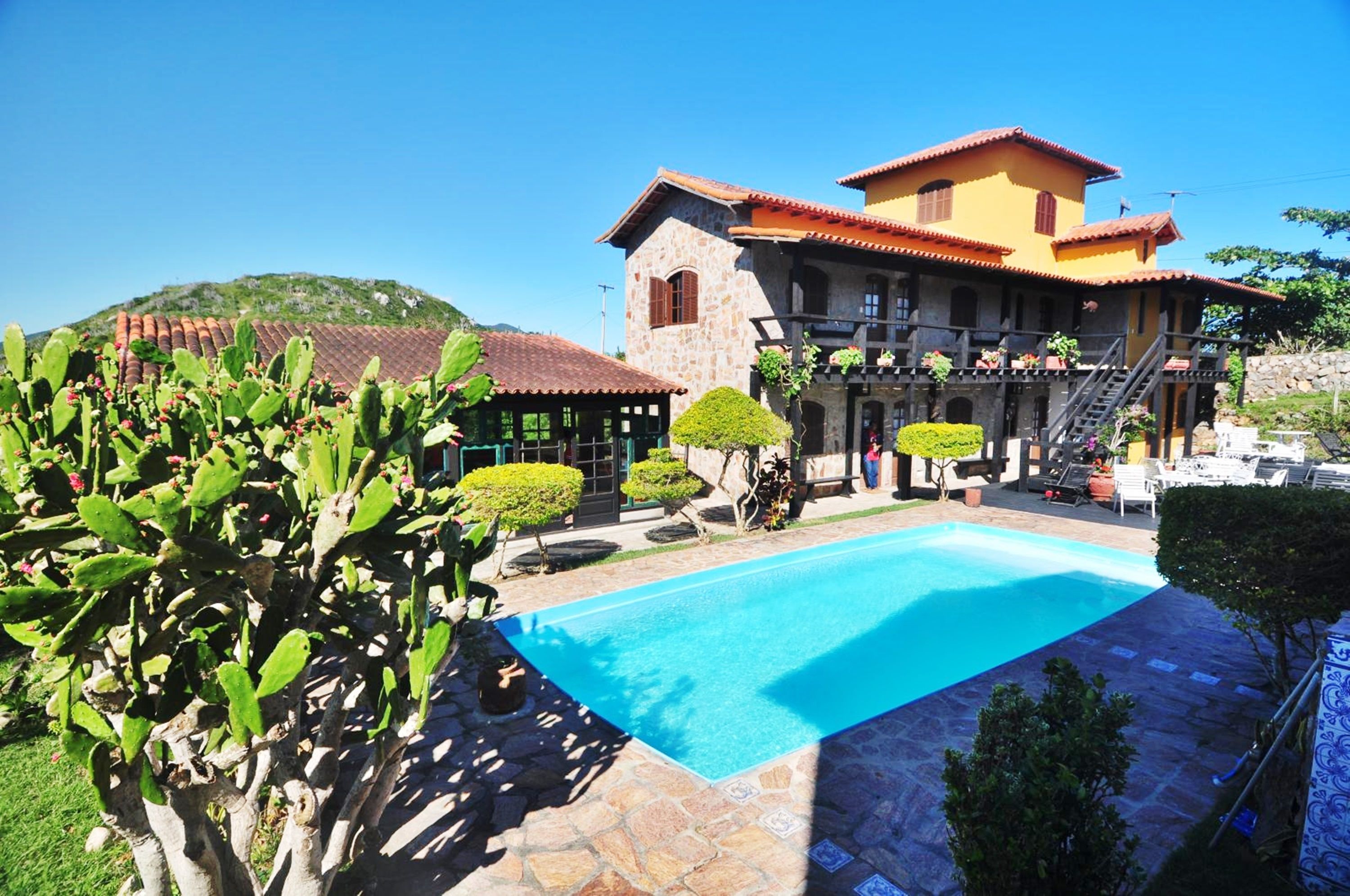 Une grande maison avec une piscine, entourée de verdure et avec une montagne en toile de fond.