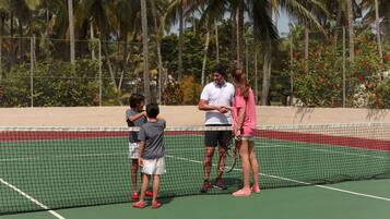 A tennis court with a net, surrounded by a fence and palm trees.
