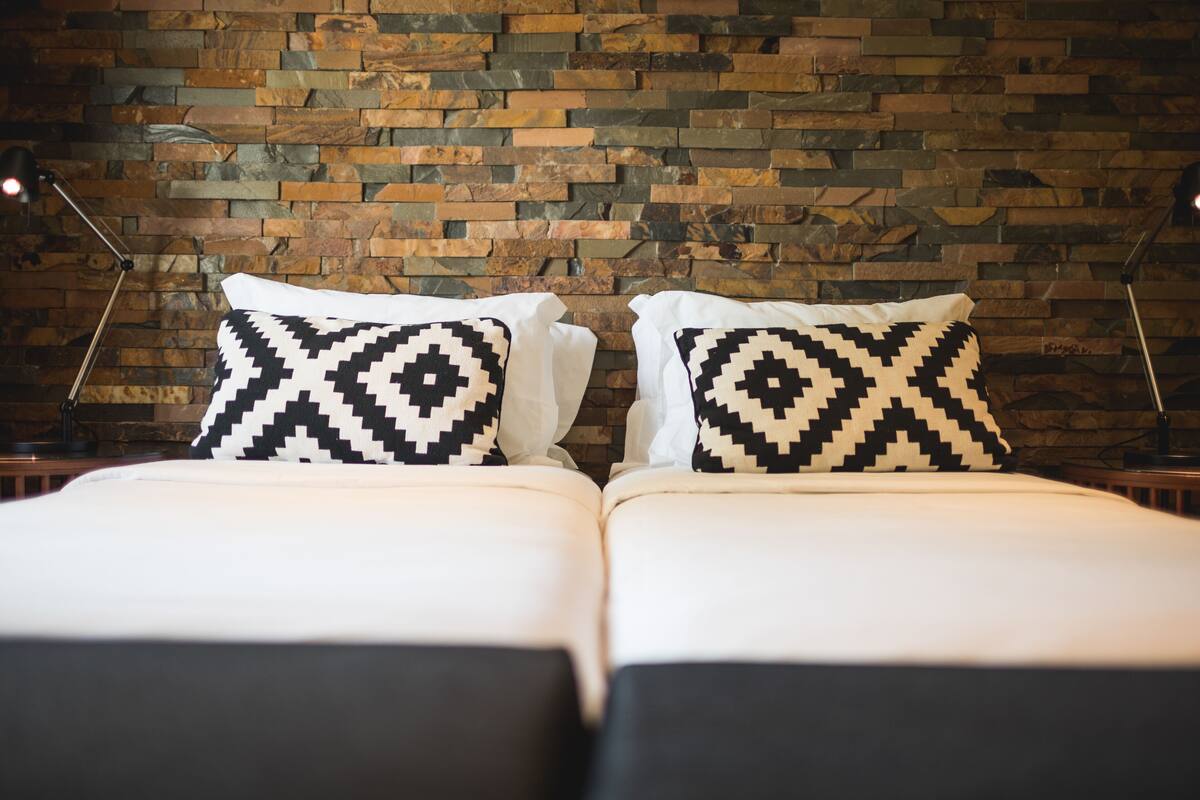 Ein Doppelbett mit gemusterten Kissen vor einer Steinwand.