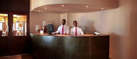 A reception desk with two staff members, a computer, and a telephone.