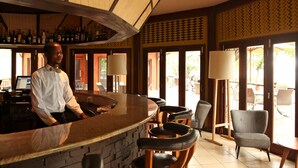 Uma área de bar com um bartender, balcão, banquetas e vista para a área externa.