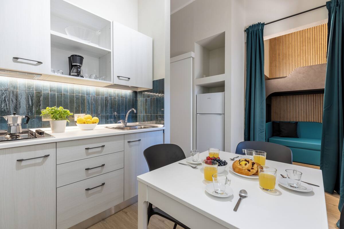 A modern kitchen with white cabinets, a coffee machine, and a breakfast setup with fruits and juice.