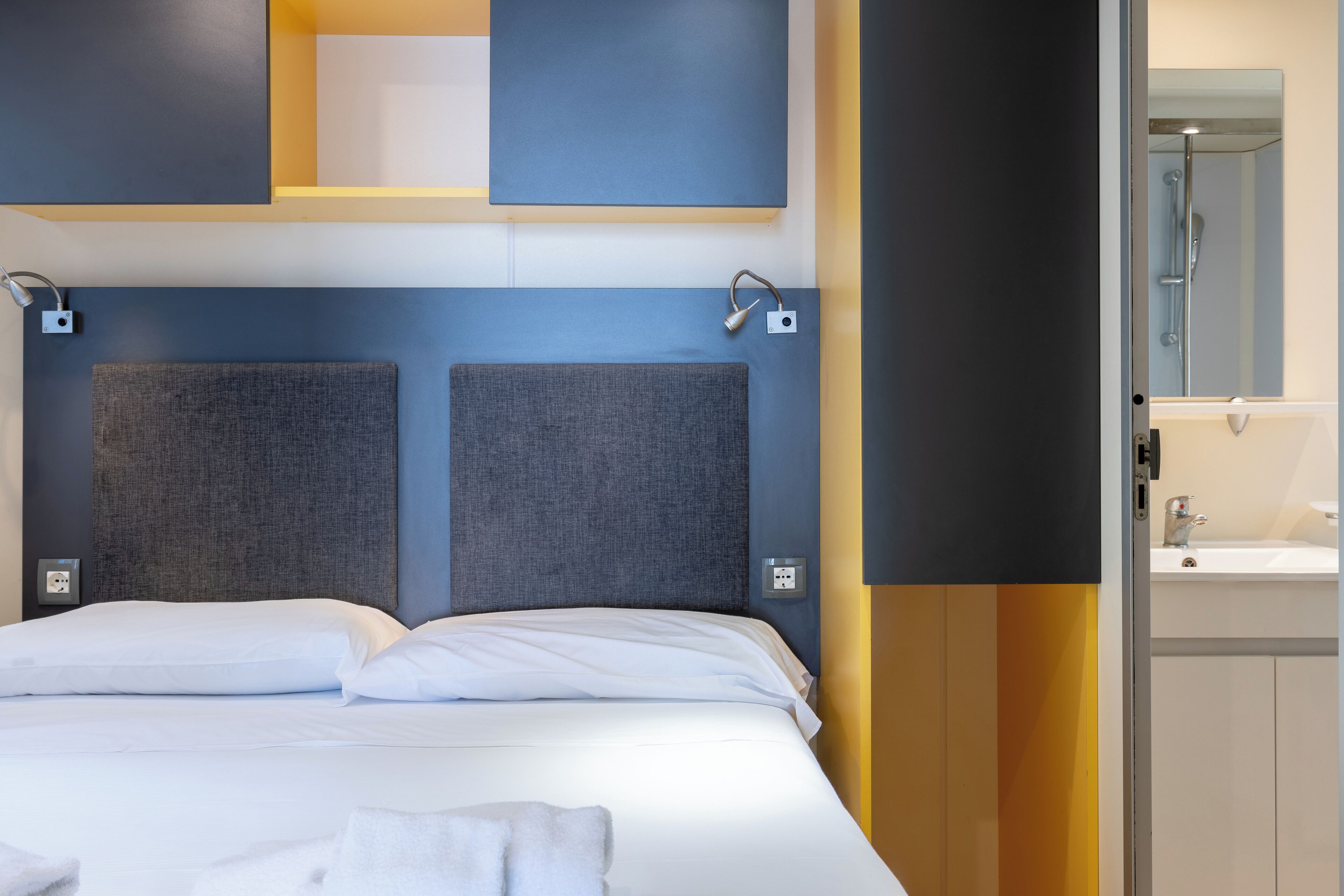 Une chambre d’hôtel moderne avec un grand lit, une tête de lit au motif texturé, une table de chevet avec une lampe et une vue sur la salle de bain.