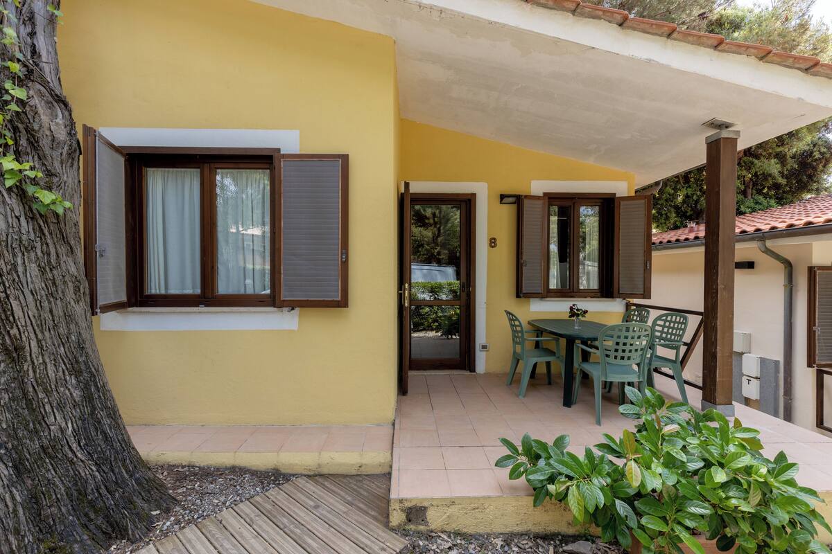 A yellow building with a covered patio, a table with chairs, and a door.