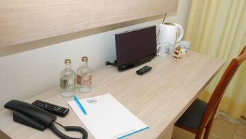 Ein Schreibtisch im Hotelzimmer mit einem Laptop, Fernbedienungen, einem Telefon, einem Notizblock und zwei Wasserflaschen.