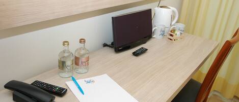 A hotel room desk with a laptop, remote controls, a telephone, a notepad, and two bottles of water.