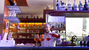 Un espace bar avec un barman qui prépare des boissons, des étagères remplies de bouteilles d’alcool et une vue sur l’extérieur.