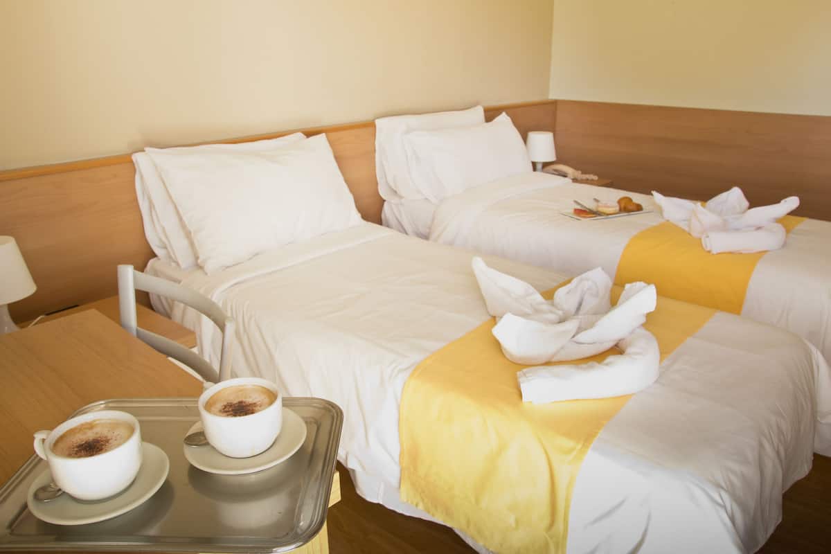 Une chambre d’hôtel avec deux lits, un plateau avec deux tasses de café et une table avec une lampe.