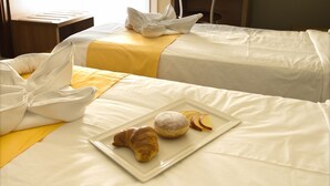 Une chambre d’hôtel avec deux lits, chacun agrémenté d’une serviette blanche soigneusement pliée et d’une couverture jaune. Une assiette contenant un croissant et des tranches de pomme est posée sur l’un des lits.