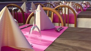 Une table à manger recouverte d’une nappe rose, avec des chaises en bois et un verre à vin.