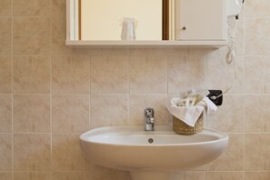 Een badkamer met een wit wastafelmeubel, een spiegel erboven en een telefoon bevestigd aan de muur.