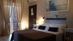 A hotel room with a large bed, a bedside table, a nightstand, a wall-mounted air conditioner, a painting, and a window with curtains. - B&B Giorgia Airport (Fiumicino)