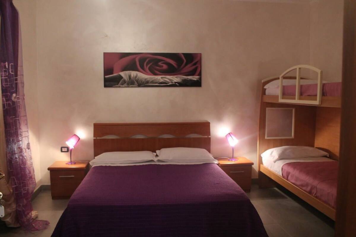 Een slaapkamer met een enkel bed, twee nachtkastjes met lampen, een stapelbed en een aan de muur bevestigd schilderij.