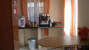 A kitchen with a coffee machine, a trash bin, and a table with a vase of flowers. - B&B Giorgia Airport (Fiumicino)