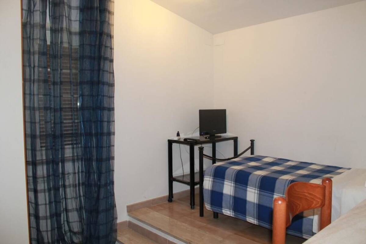Een kleine kamer met een bed, een tafel met een televisie en een stoel.