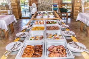 Enjoy a delicious breakfast spread with a variety of options, including eggs, sausages, and salads, served in a rustic dining area with tables and silverware.