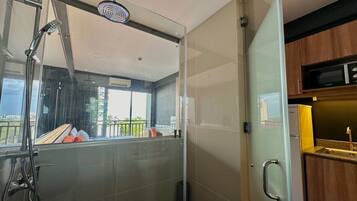 A modern bathroom with a glass shower enclosure, a visible balcony, and a kitchen area with wooden cabinets.
