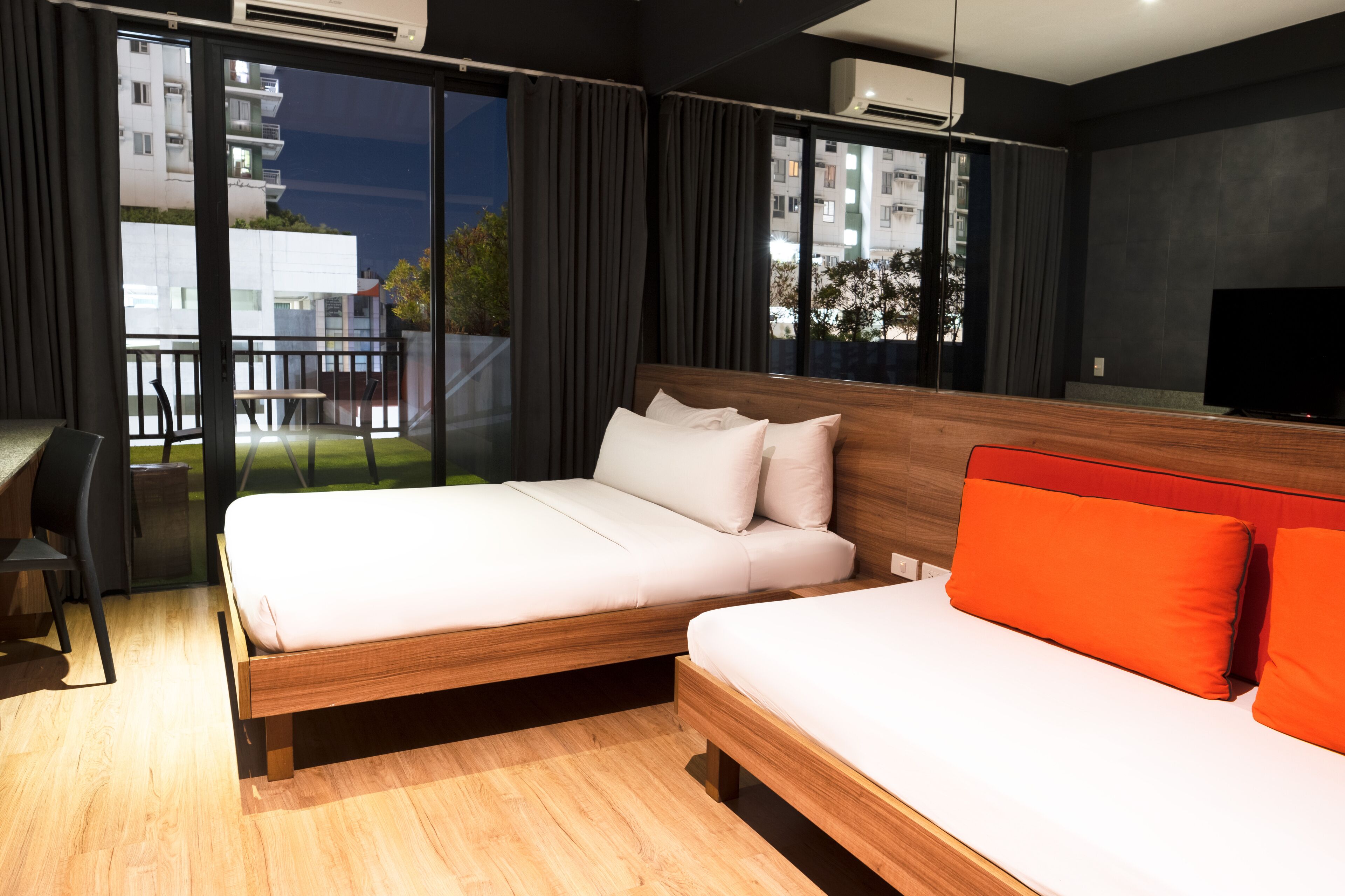A modern hotel room with a large bed, a smaller bed, a desk, and a TV.