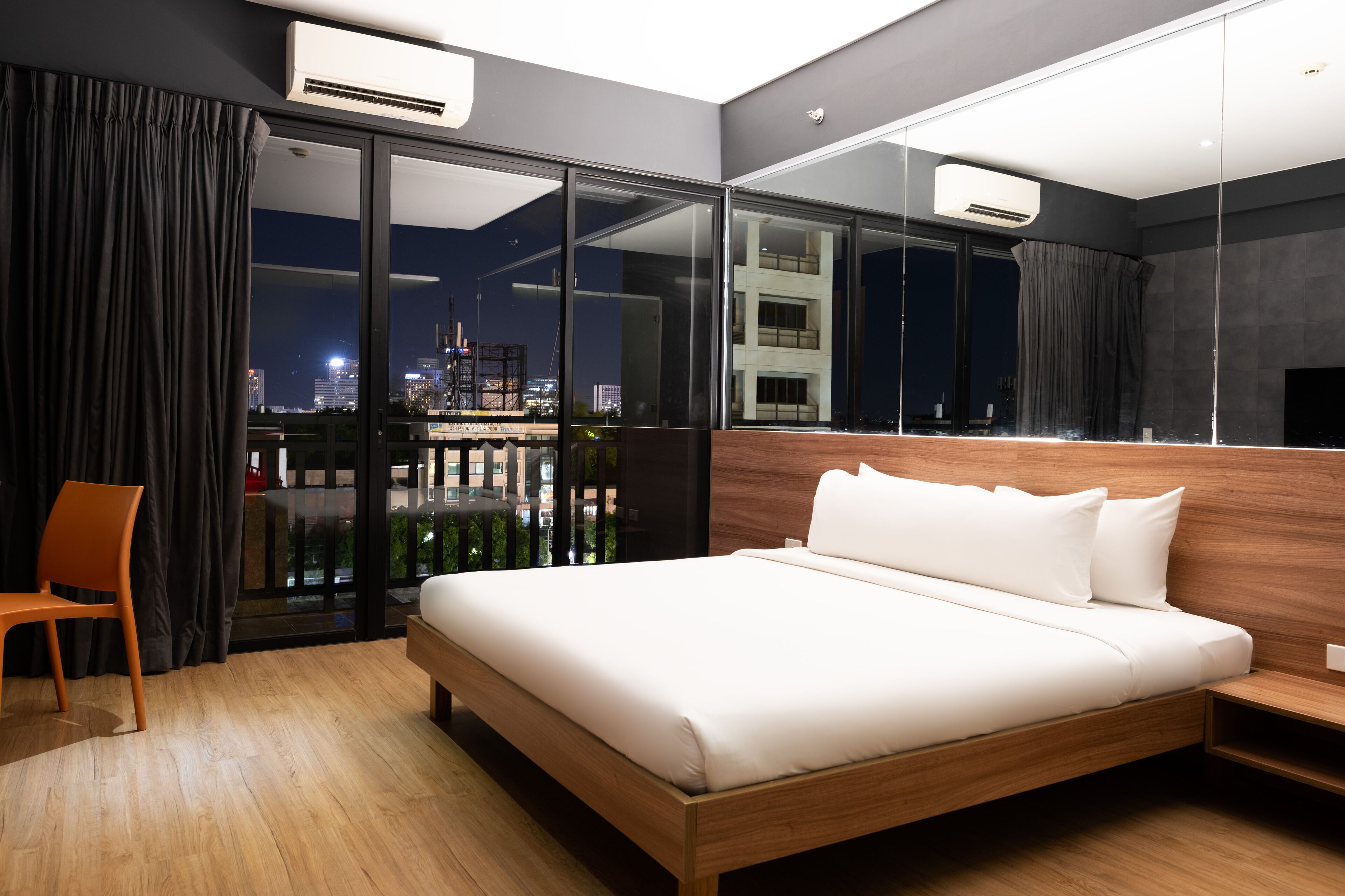 A modern hotel room with a large bed, a chair, a desk, and a balcony with a city view.