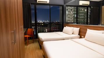 Habitación de hotel con dos camas, una silla y un amplio ventanal con vista a la ciudad.