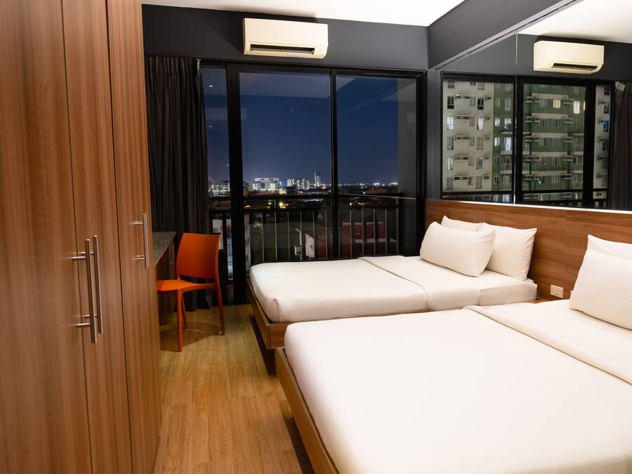 Habitación de hotel con dos camas, una silla y un amplio ventanal con vista a la ciudad.