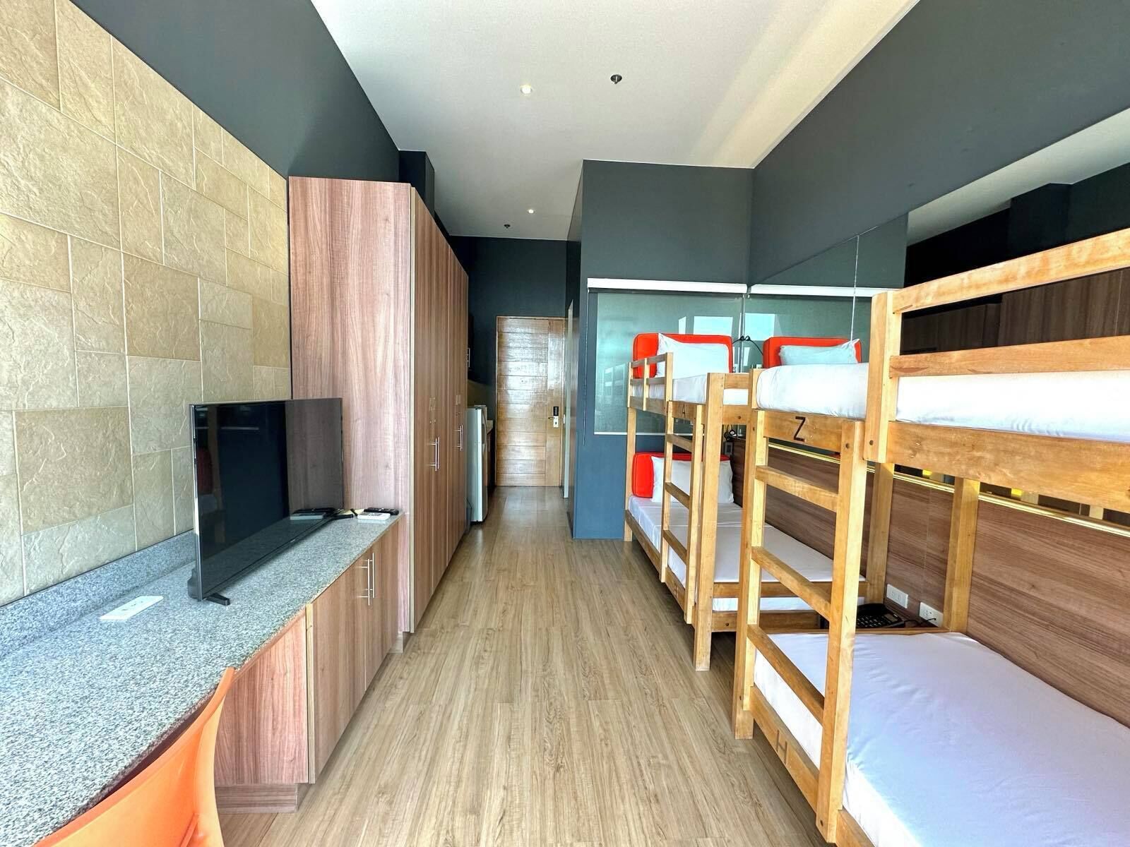 A modern hotel room with bunk beds, a flat-screen TV, a kitchenette, and a large window.