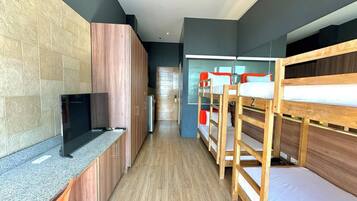 A modern hotel room with bunk beds, a flat-screen TV, a kitchenette, and a large window.