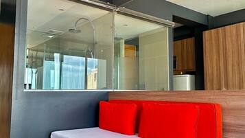A modern bedroom with a large mirror, a bed with red pillows, and a view of a shower and kitchen area.