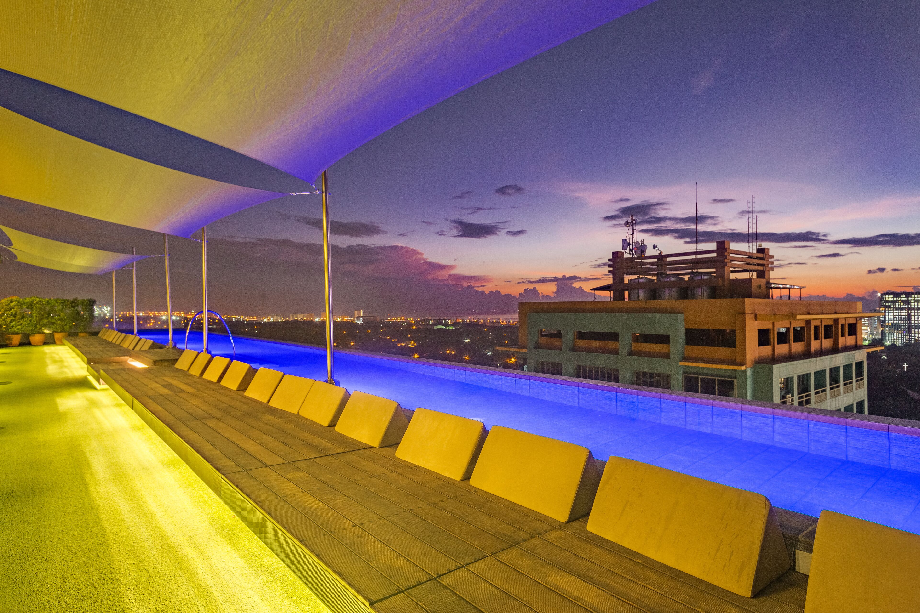 Zona de piscina en la azotea con vista al horizonte urbano al anochecer.