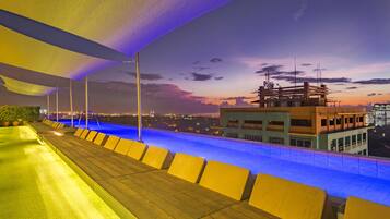 Zona de piscina en la azotea con vista al horizonte urbano al anochecer.