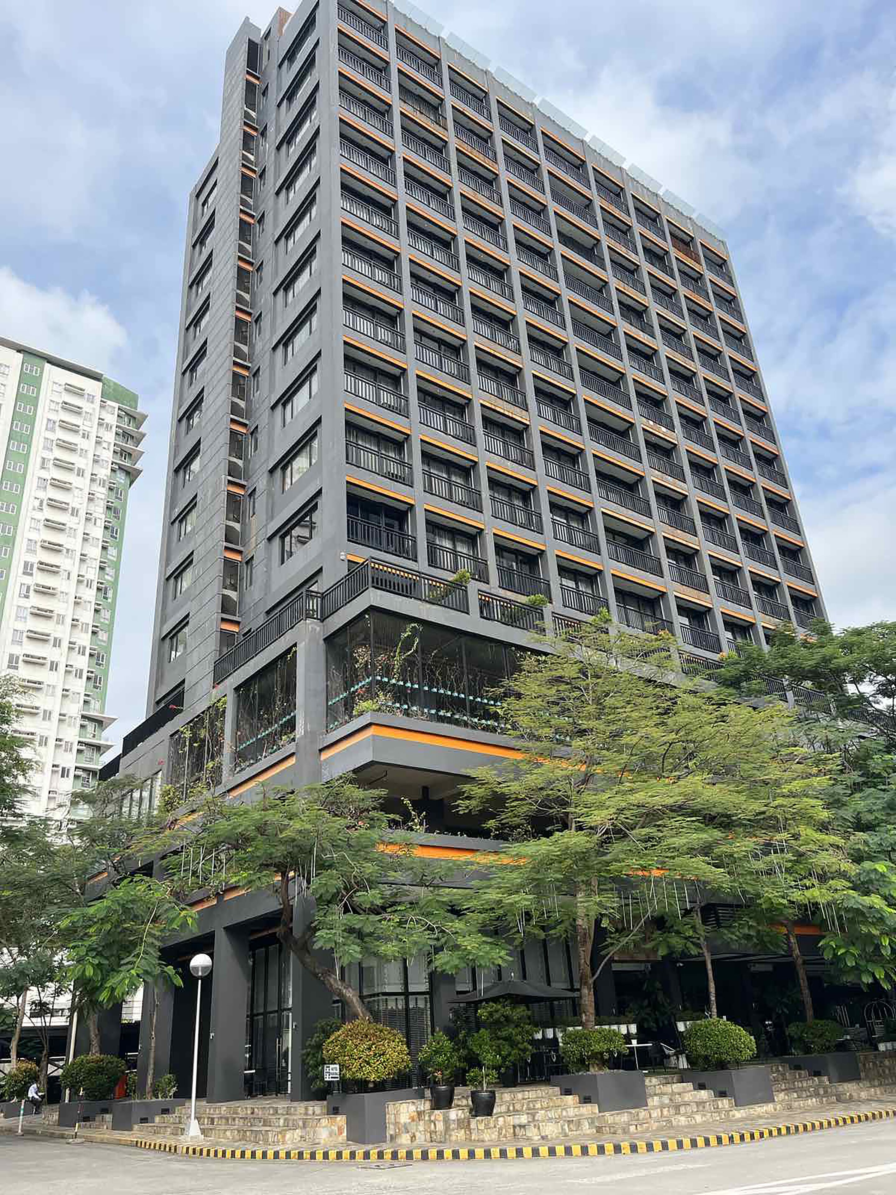 A high-rise building with multiple balconies, surrounded by greenery and a clear sky.