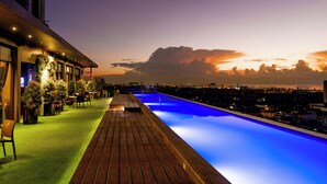 A rooftop pool with a wooden deck and seating area, overlooking a cityscape at sunset. - Azumi Boutique Hotel (Muntinlupa)