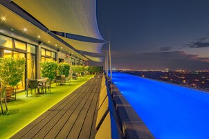Un bar en la azotea con piscina, mesas al aire libre y vistas a la ciudad al anochecer.