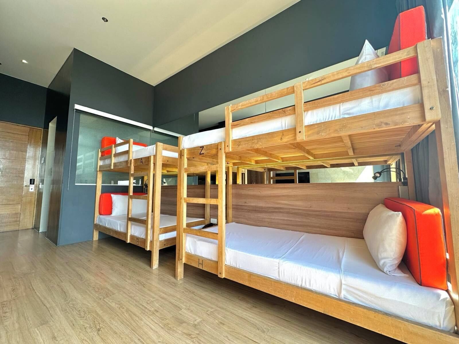 Dormitorio con literas de madera, ropa de cama blanca y cojines rojos.