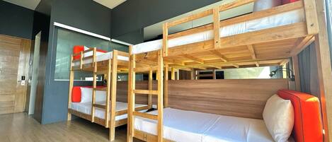 Dormitorio con literas de madera, ropa de cama blanca y cojines rojos.