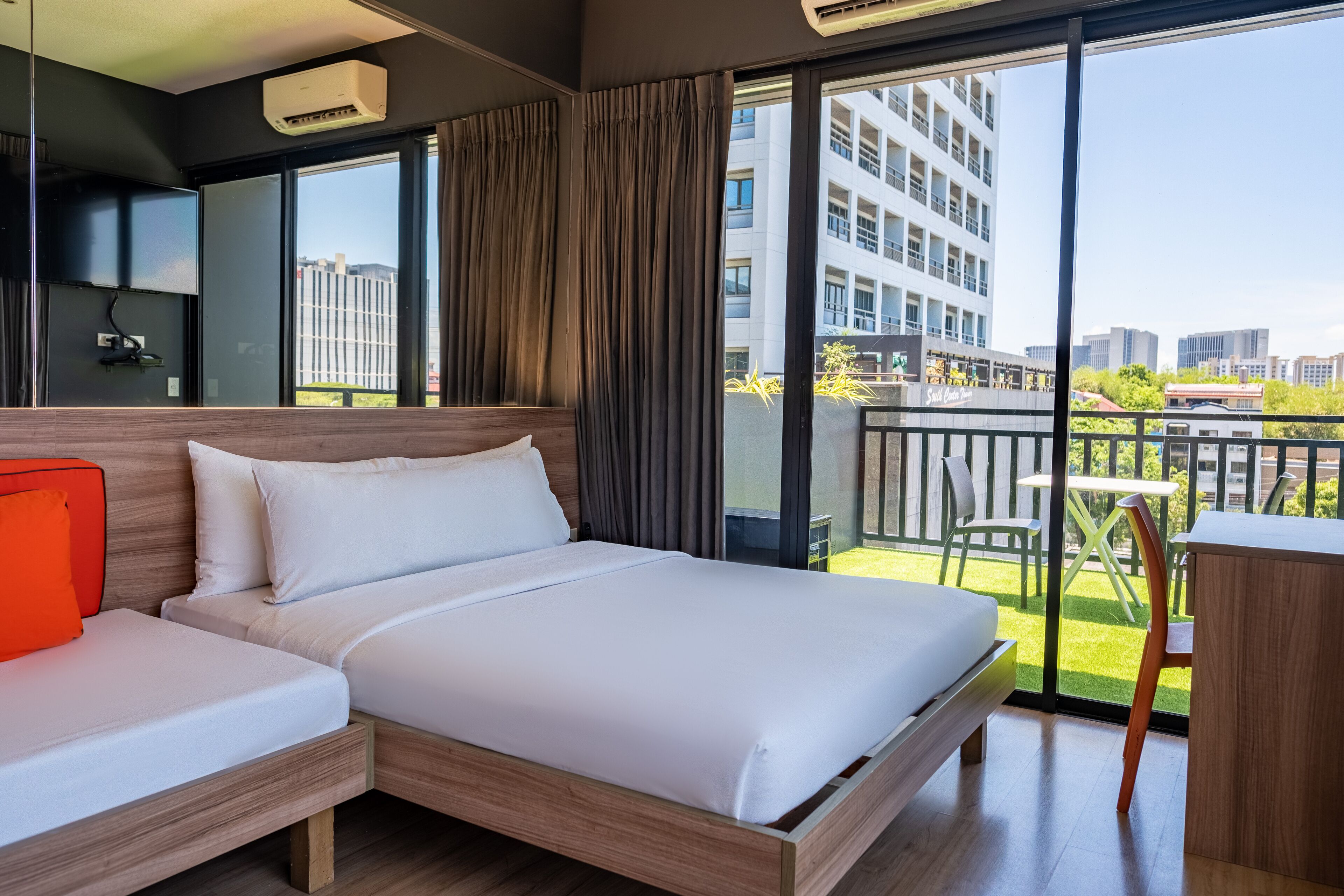 Una habitación de hotel moderna con una cama grande, un escritorio y un balcón con vistas a la ciudad.