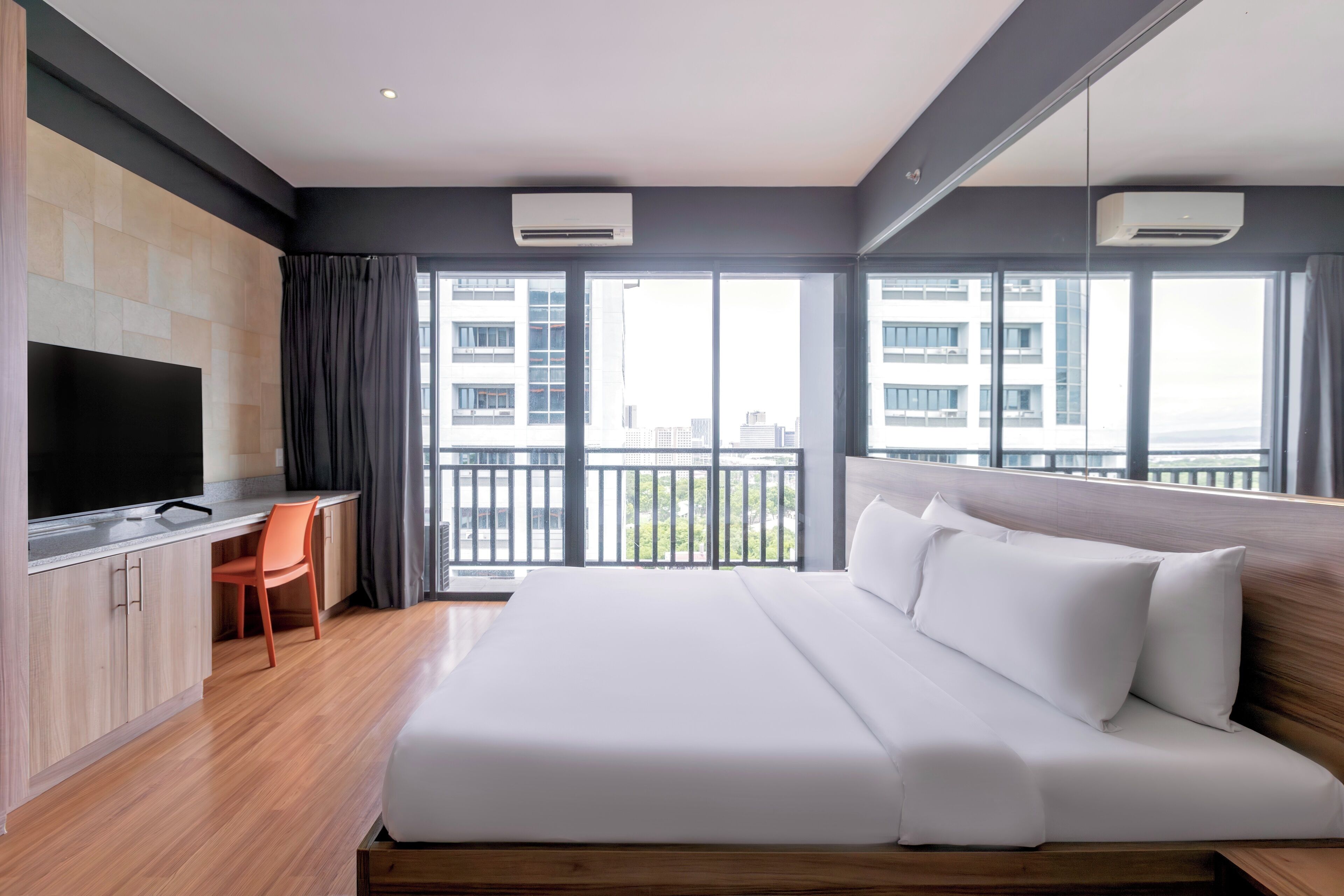 Habitación de hotel moderna con una cama grande, un escritorio con silla, un televisor de pantalla plana y un balcón con vistas a la ciudad.