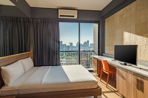 Una habitación de hotel moderna con una cama grande, un escritorio con televisor de pantalla plana y vistas a la silueta urbana a través de un ventanal amplio.