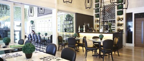 A modern restaurant with black leather chairs, a bar area with shelves of bottles, and a checkered floor.