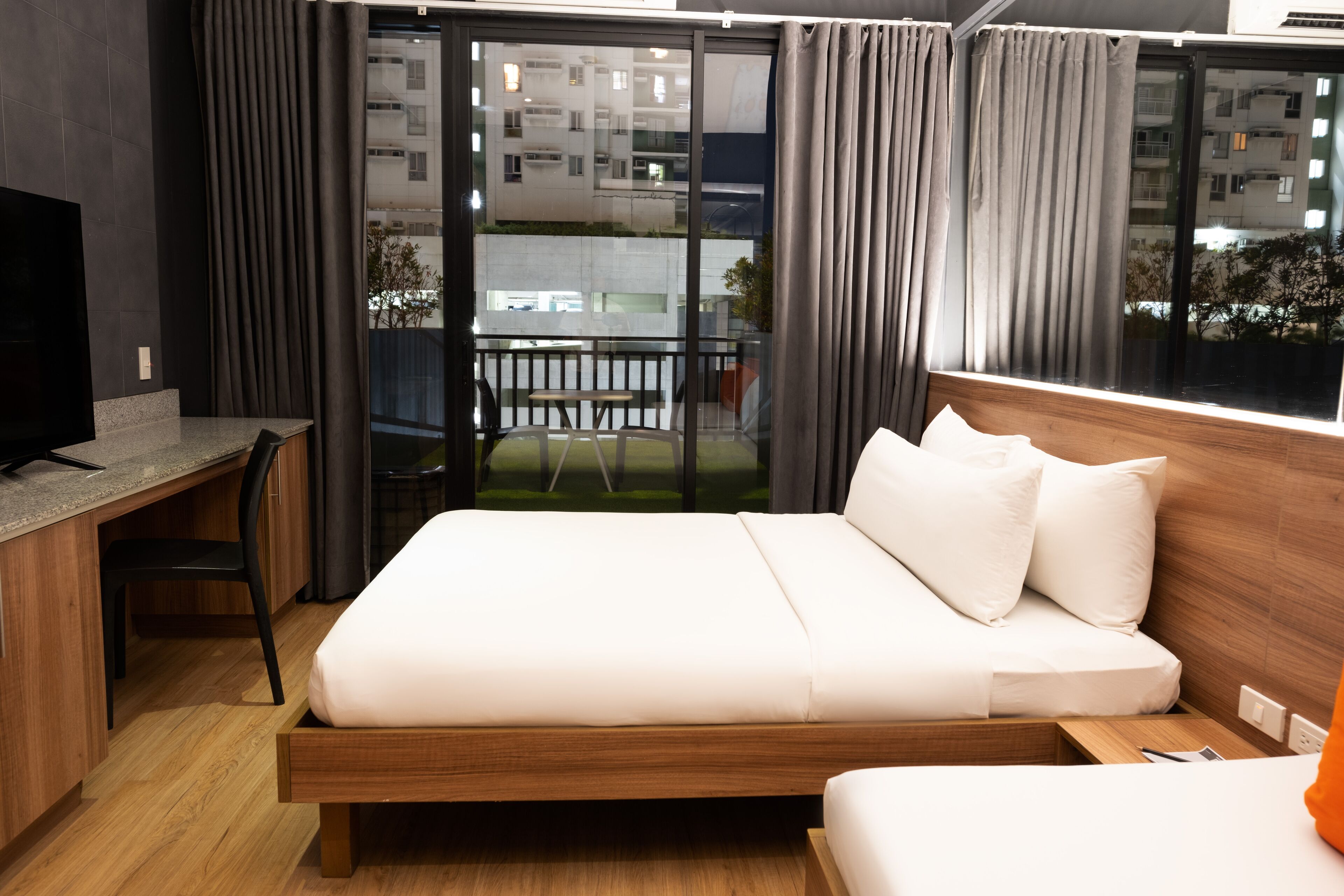 A modern hotel room with a wooden bed, a desk, and a large window with curtains.