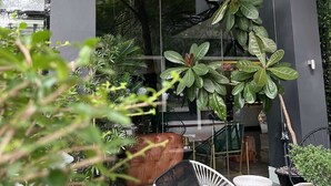 The exterior of Azumi Boutique Hotel with a stone facade, large windows, and outdoor seating area with chairs and potted plants. - Azumi Boutique Hotel (Muntinlupa)