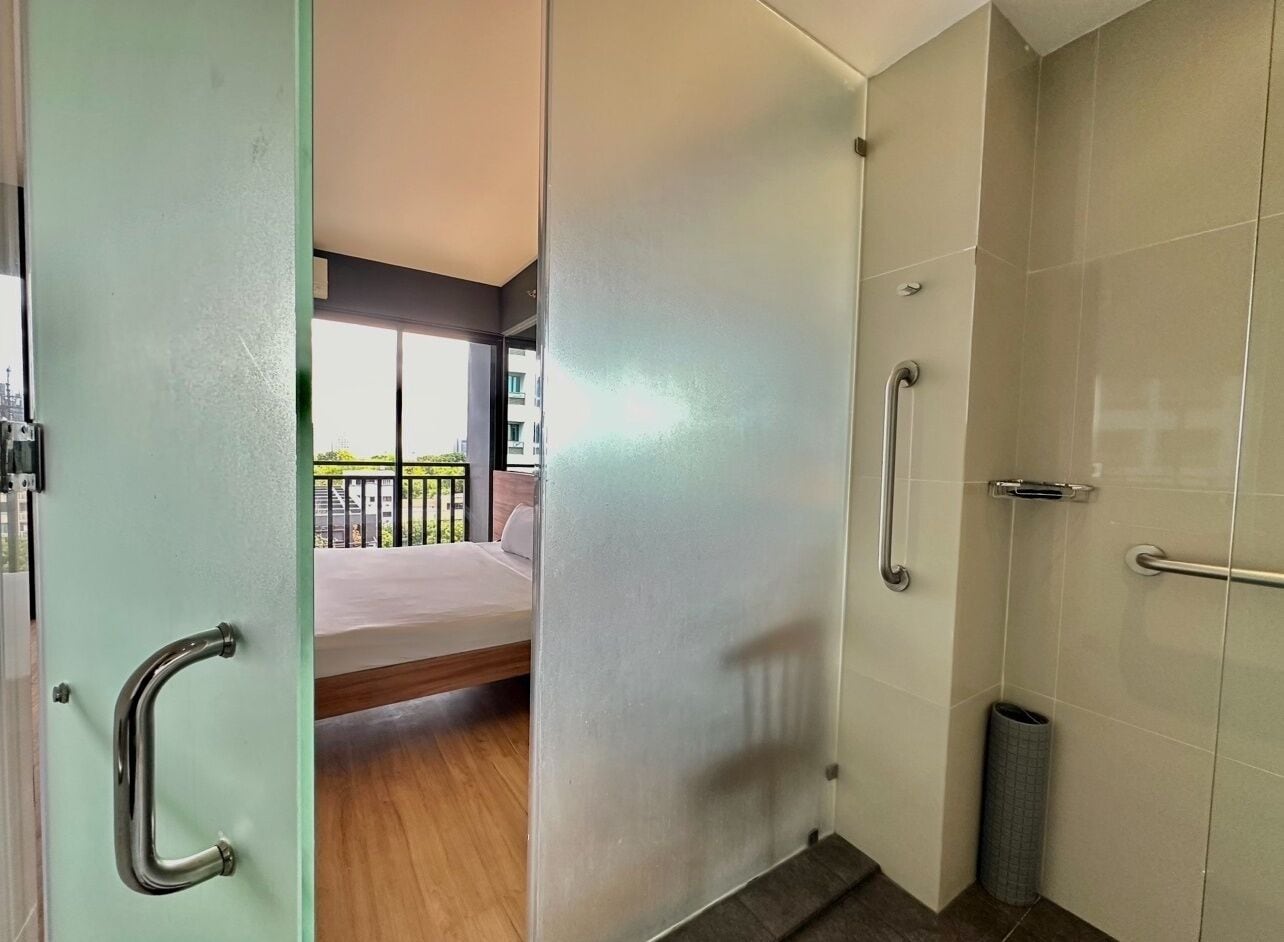 A modern hotel room with a bed, a bathroom with a shower, and a balcony with a railing.