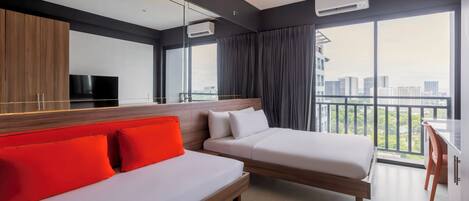 A modern hotel room with a large bed, a sofa with red cushions, a TV, and a balcony with a city view.