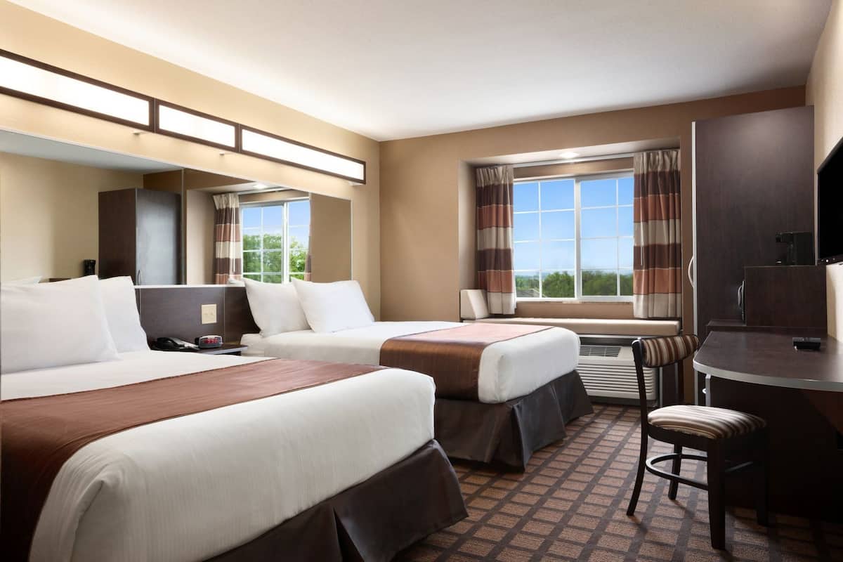 A hotel room with two beds, a desk, a chair, a TV, and a window with curtains.