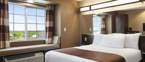 A hotel room with a large bed, a window seat, a desk, and a mirror.